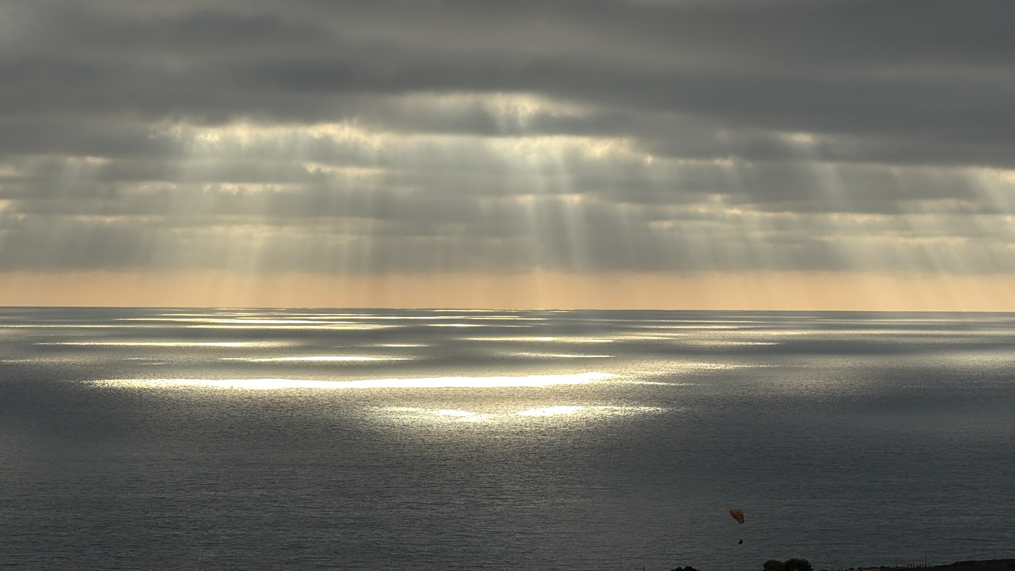 Paraglider beneath sunbeams over the Pacific Ocean
