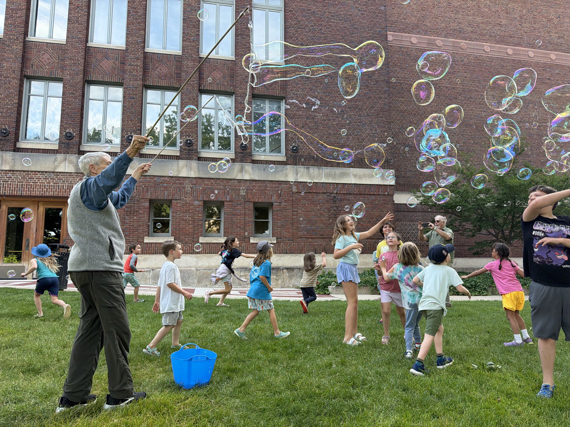 Children chasing giant soap bubbles on a campus lawn in Ann Arbor
